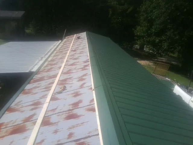 Old rusted panels beside newly installed green metal roofing — Wind Damage Roof Repair by Roofing Brothers in New Richmond