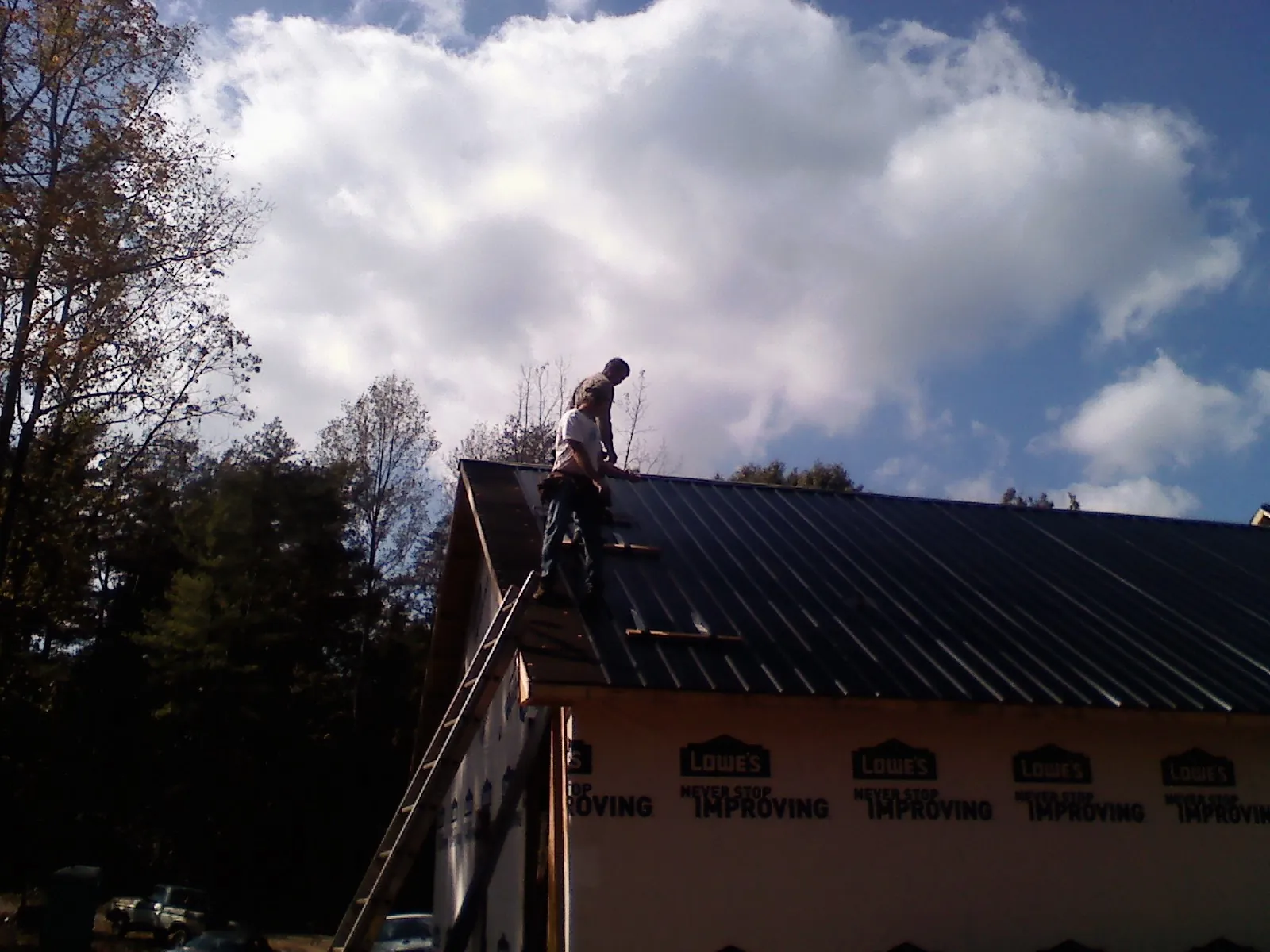 Roofer fastening dark metal panels high against a cloudy sky, from a Roof Inspection job in New Richmond