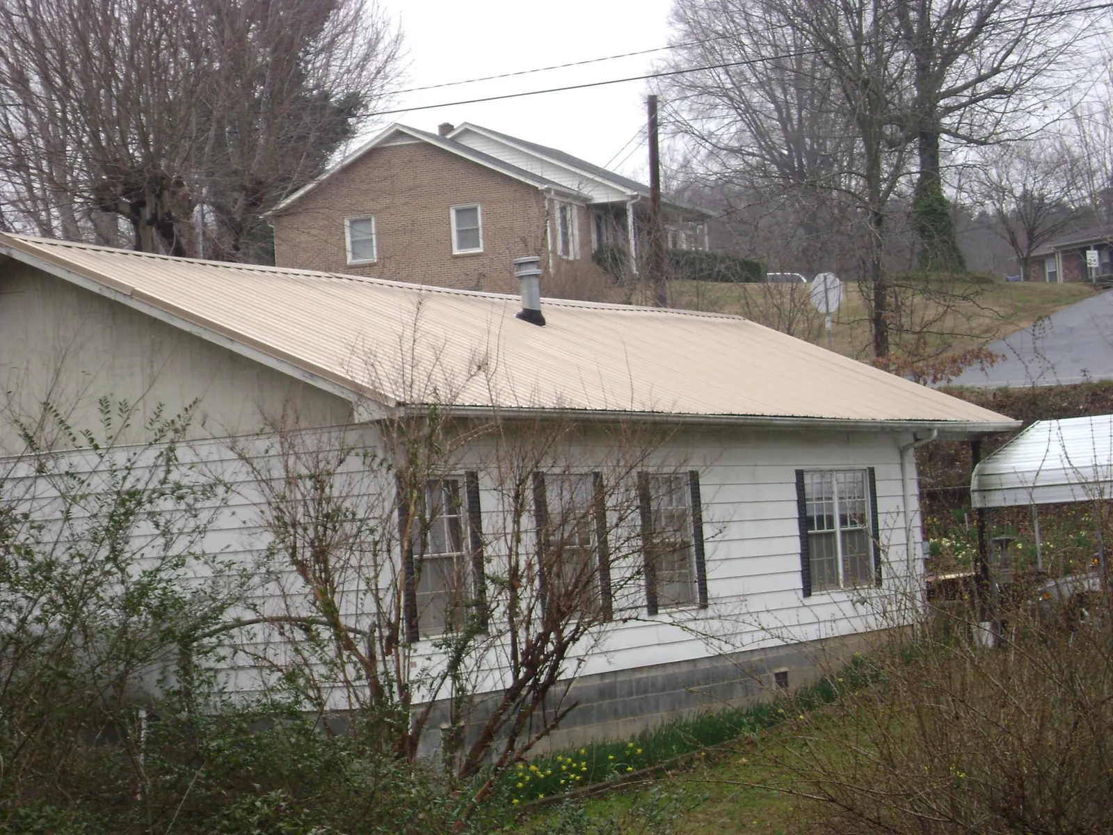 Tan metal roof on a white sided house set into a hillside — Commercial Roofing by Roofing Brothers in New Richmond